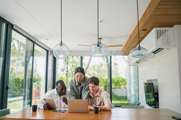 A multi-ethnic group of young adults collaborates using a laptop in a bright, well-lit office...