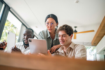 A group of young adults of varying ethnicities collaborate on tablets in a well-lit, modern office space, their professional attire suggesting a business environment.