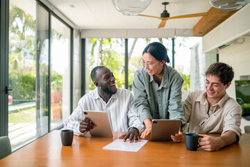 Fototapeta premium A diverse group of young adult professionals engaging in a discussion over documents and digital tablets, dressed in casual business attire, in a bright, contemporary office space.