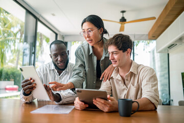 A young, diverse group of professionals collaborates using digital tablets and documents at a sleek wooden table, reflecting teamwork in a contemporary office environment.
