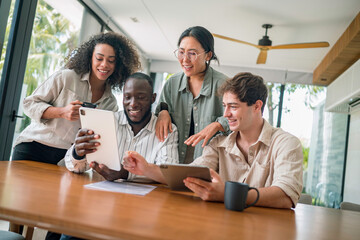 A group of young adults of various ethnicities collaborate around a tablet in a modern office, showcasing teamwork and technology integration.