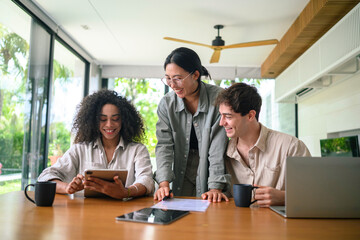 Three young adults display teamwork as they review content on a digital tablet, discussing strategies in their light-filled office, with modern design elements enhancing their collaboration.