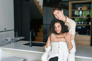 Fototapeta premium A cheerful young African American woman and her Caucasian partner embrace in a cozy kitchen, reflecting joy and unity in their casual outfits.