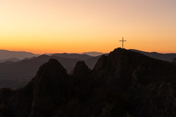 Christian cross on top of a mountain in Georgia against the backdrop of a picturesque fiery sunset