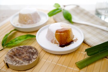 Ein traditionelles asiatisches Dessert mit Sago-Pudding, serviert mit Kokosmilch und Palmzuckersirup, schön angerichtet auf einer Bambusmatte mit frischen Pandanblättern.