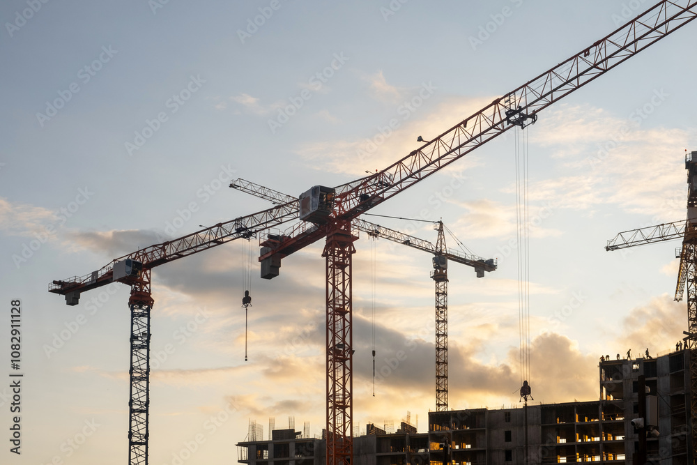 Aufkleber cranes loom at a construction site against a colorful sunset, as workers engage in various tasks to 