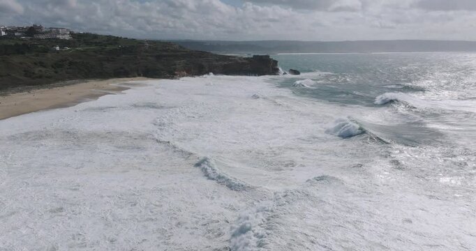 Aerial drone shot of big waves breaking on rocks and cliffs on a day with giant waves in Nazare, Portugal, Europe. Farol da Nazar&eacute; lighthouse visible. Shot in ProRes 422 HQ