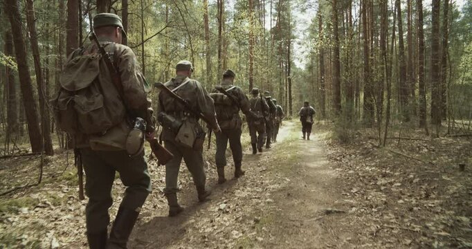 Reenactment Tactic Game. Group Of Reenactors Dressed As German Infantry Soldiers Marching By Forest Road Autumn Season. Wermacht German Military Uniform And Rifle During Ww2. Carabin Mauser 98k