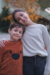 Two cute kids in casual clothes hug and pose for camera. Brother and sister smile and have good time together.
