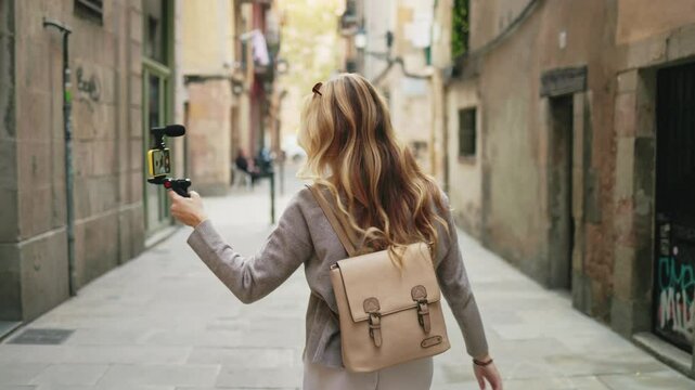 Travel influencer recording content with her smartphone gimbal while walking in a narrow street.   Influencer walking and filming with smartphone gimbal