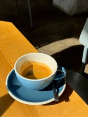 Morning espresso in a blue cup with natural sunlight casting shadows on a wooden table