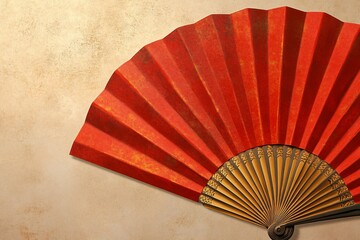 Close-up of a red folding fan with golden accents on a textured beige background