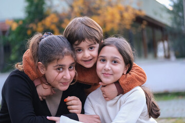 A happy moment between two  sisters and their brother. The older siblings are hugging the little brother.