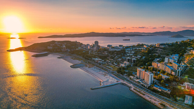 Sunset aerial view of Ela Beach in Port Moresby from Koki with the horizon just before the sun disappears, giving a beautiful golden reflection on the water and boats anchored in Fairfax Harbour