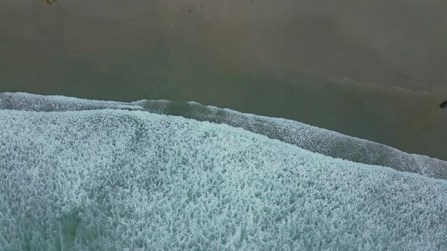 Aerial footage of the Atlantic Ocean waves lapping on a sandy shore in Cayon city, A Laracha, Spain