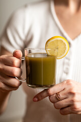 Kratom consumption concept:  female holds a ready to drink glass of green liquid, powdered kratom...