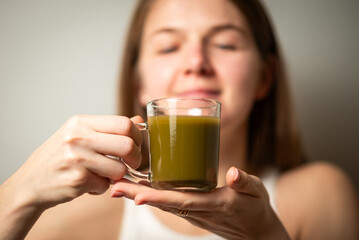 Kratom consumption concept:  female holds a ready to drink glass of green liquid, powdered kratom...