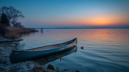 Fototapeta premium Wooden canoe on serene lake at sunrise with vibrant reflections and a tranquil reed-lined shore
