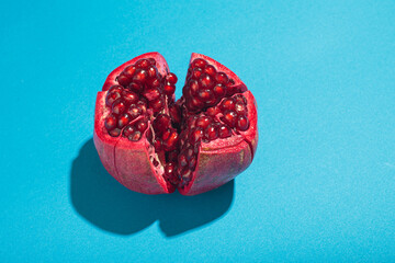 Ripe pomegranate, bursting open to reveal its juicy red seeds, on a vibrant blue background,...