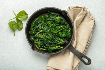 Freshly steamed spinach leaves are served in a cast iron pan, resting on a beige napkin, healthy...