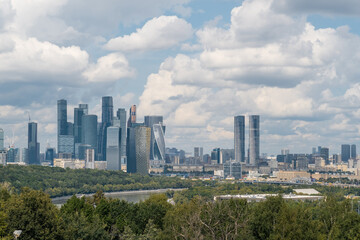 Fototapeta premium Visitors enjoy the lush greenery of Luzhniki Park while taking in the impressive Moscow City skyline with clouds above