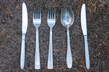 set of metal gray forks spoons and knives lie on the ground on a summer street