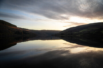 Obraz premium Calm lake reflecting cloudy sky at sunset in autumn