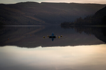Calm lake reflecting mountains and autumnal colors at sunset with buoys and small platform