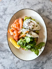 Healthy food. Toast with avocado, smoked salmon and poached eggs. Breakfast or lunch in a cafe on a marble table