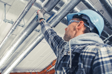Man in Safety Gear Inspecting Overhead Pipes in a Construction Site During the Day