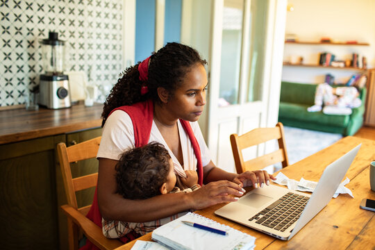 Working mom multitasking with baby on lap at home office setup