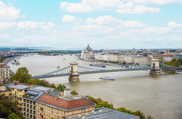 Obraz premium On a sunny, summer day, sightseeing boat tours travel near the Hungarian Parliament and the Széchenyi Chain Bridge that spans the Danube River and connects Buda and Pest in Budapest, Hungary.