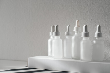 Frosted Glass Cosmetic Serum Bottles With Dropper Pipette Dispenser On White Rectangular Box, Striped Surface And Gray Background