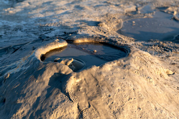Close-up of a bubbling mud pool in a volcanic area, capturing the texture and fluid motion of the mud under sunlight, highlighting the raw geothermal activity.