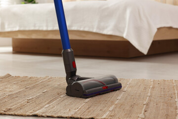 Cleaning rug with cordless vacuum cleaner indoors, closeup