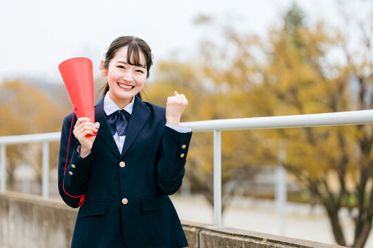 メガホンを持ってガッツポーズするブレザー姿の女子学生（応援・エール・声援・青春）
