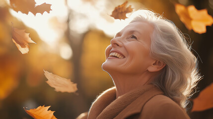 Happy senior woman enjoying falling autumn leaves in golden forest