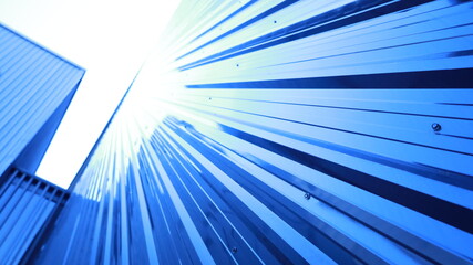 Blue corrugated metal sheet wall. Shiny corrugated iron sheets partition the wall of a modern building in an angle with sunlight shining above in a bottom view with copy space. Selective focus