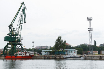 Fototapeta premium Varna port coastal view, green portal crane is under bright cloudy sky