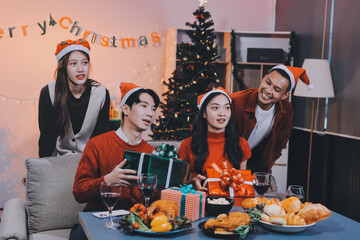 Group of young Asian man and women as friends having fun at a New Year's celebration, holding gift...