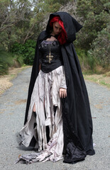 Naklejka premium full length portrait of beautiful red haired female model figure, wearing gothic fantasy costume with torn ballgown wedding dress, black corset, leather boots. walking pose forest scenery background.