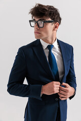 elegant young student in his 20s looking to side and buttoning suit