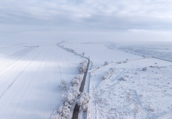 Winter landscape. Road in a field, snow on the trees, many clouds in the sky. The sun's rays break through the clouds and illuminate the snow-covered field in spots. Vivid drone photographs of natural