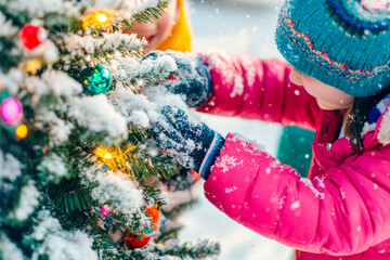 Obraz premium Close-up happy girl decorates a small Christmas tree outside in a snowy yard