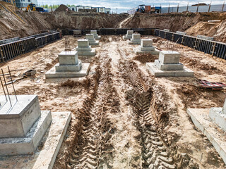Construction site with concrete foundations and machinery at work under a clear blue sky,...
