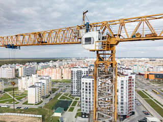 A towering crane oversees urban construction projects in a bustling cityscape on a cloudy day,...