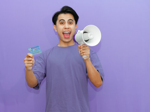 Young Asian man shouting through a megaphone while holding a resident identity card on a vibrant purple background.