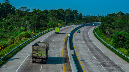 Photos of cars driving on the toll road near the mountains, indicated by the many plants under the toll road