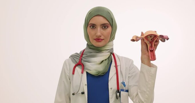 Female Muslim doctor holds colored condom pack and model of uterus. Lady in hijab encourages to use contraception against unexpected pregnancy slow motion