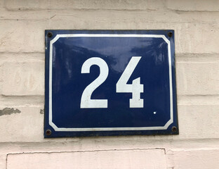 Blue metal sign that says number 24 on a white brick wall